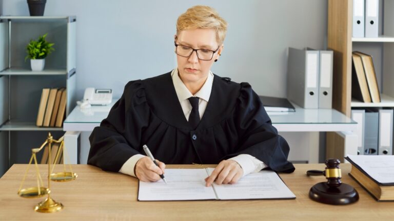 Judge serious woman in professional outfit black robe writing reviewing documents in court room